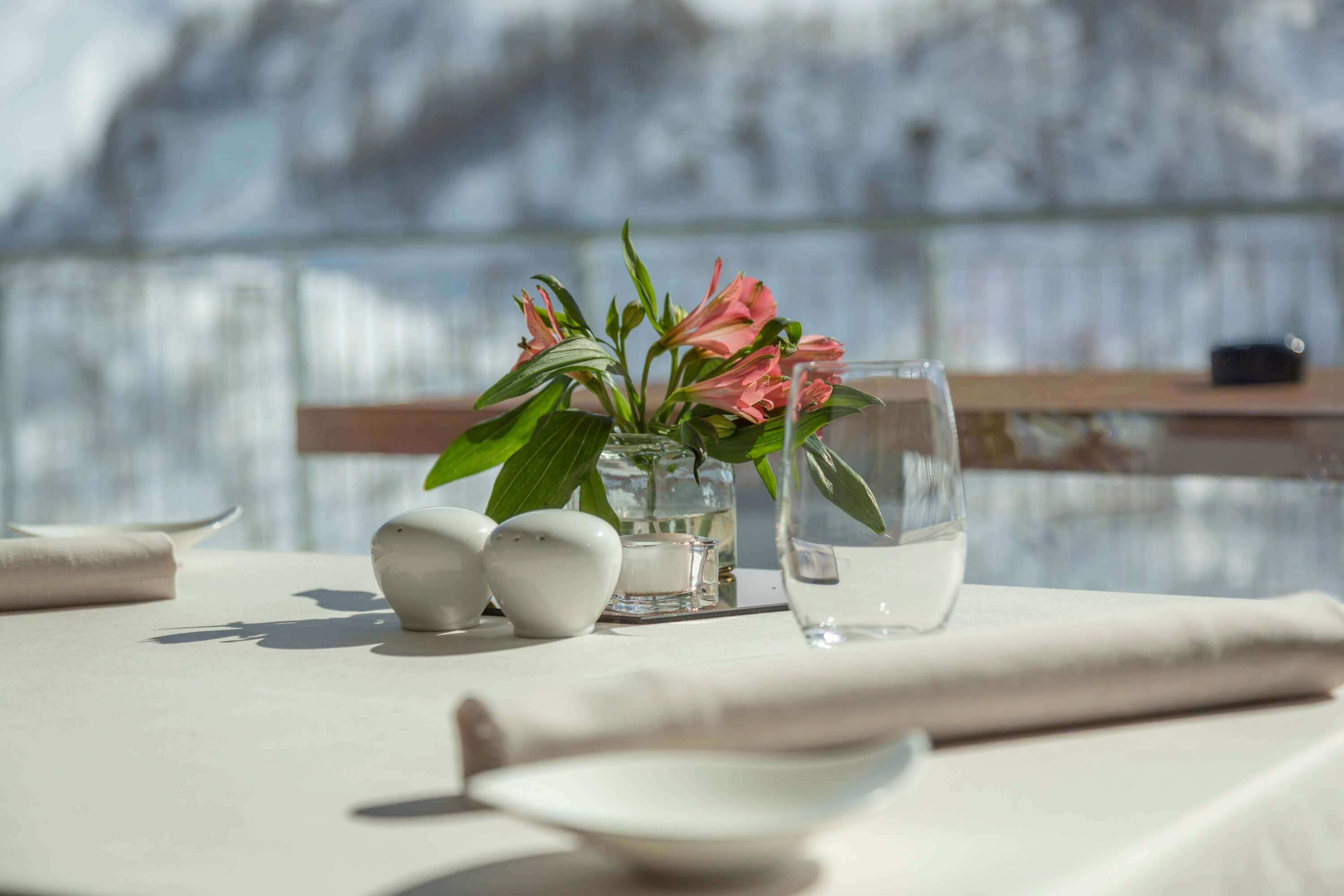 Elegant table setting with pink flowers, glassware, and white ceramics on a white tablecloth, exuding calm sophistication.